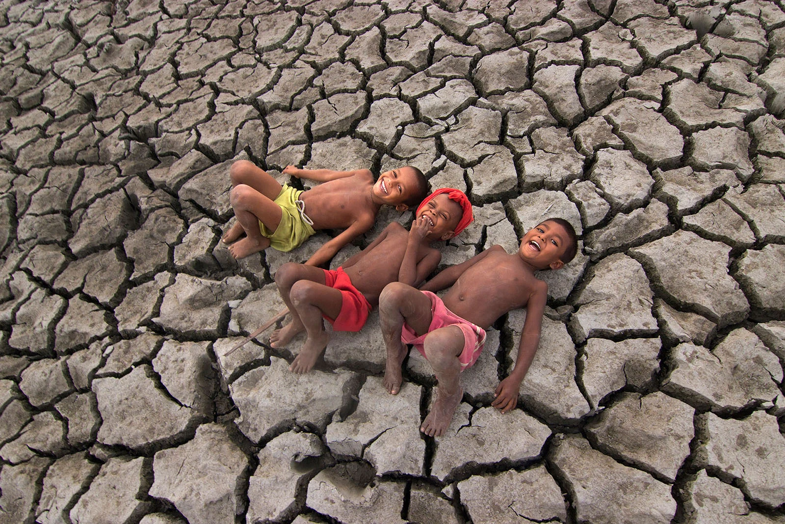 Children lying on dry, cracked earth, symbolising the impact of water scarcity and climate change