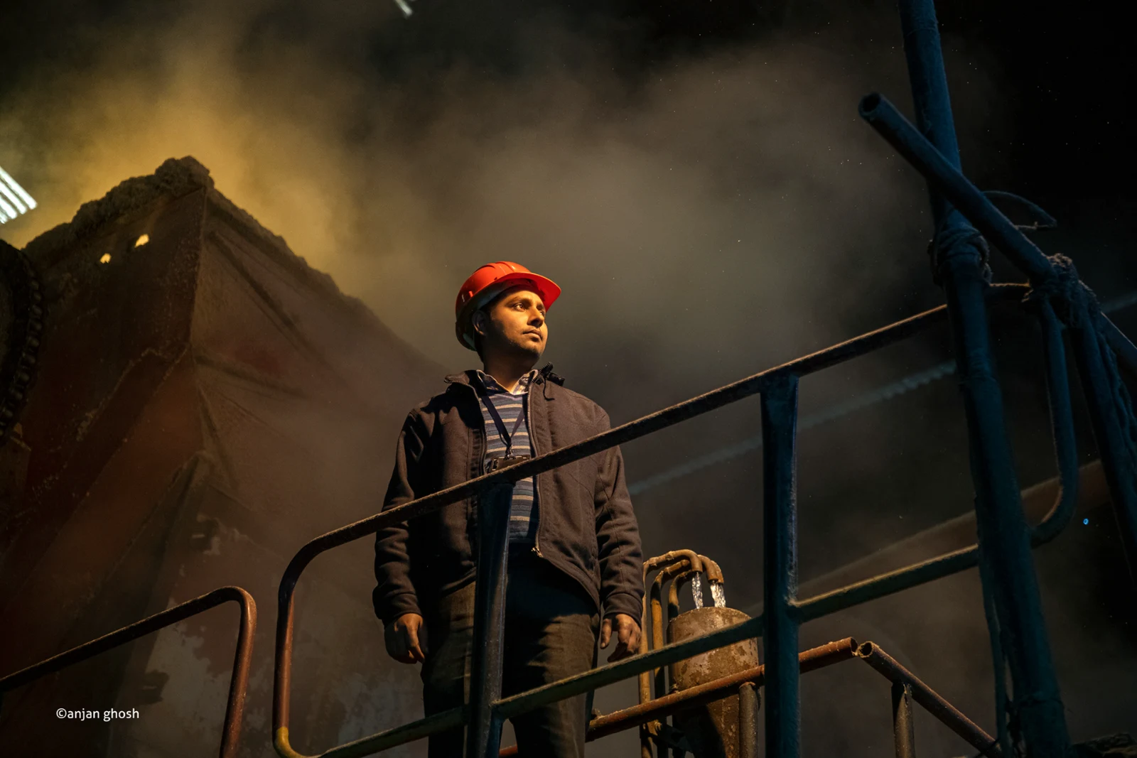 Worker standing inside a sugar manufacturing facility surrounded by industrial machinery and steam
